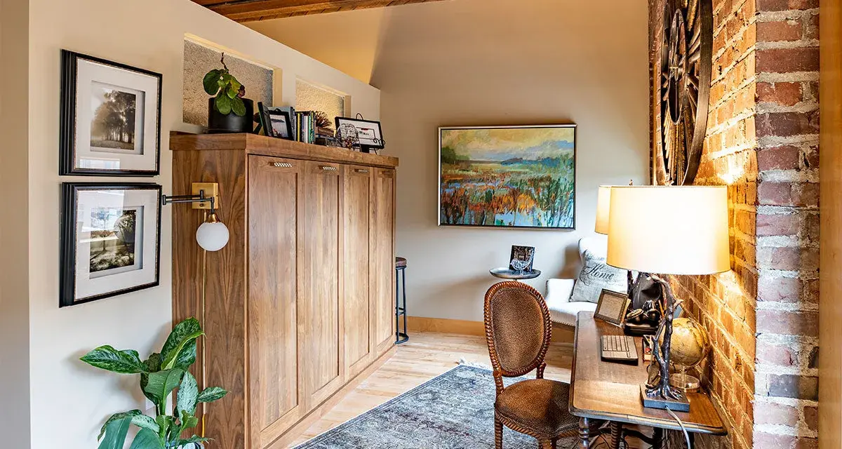 Accogliente angolo studio con un armadio a scomparsa in legno, un tappeto persiano e un quadro paesaggistico, che evoca l'atmosfera di una piccola casa di campagna.