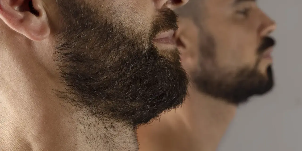 Primer plano de un hombre con barba oscura y tupida, reflejado en un espejo. La imagen captura la decisión de dejar crecer la barba.
