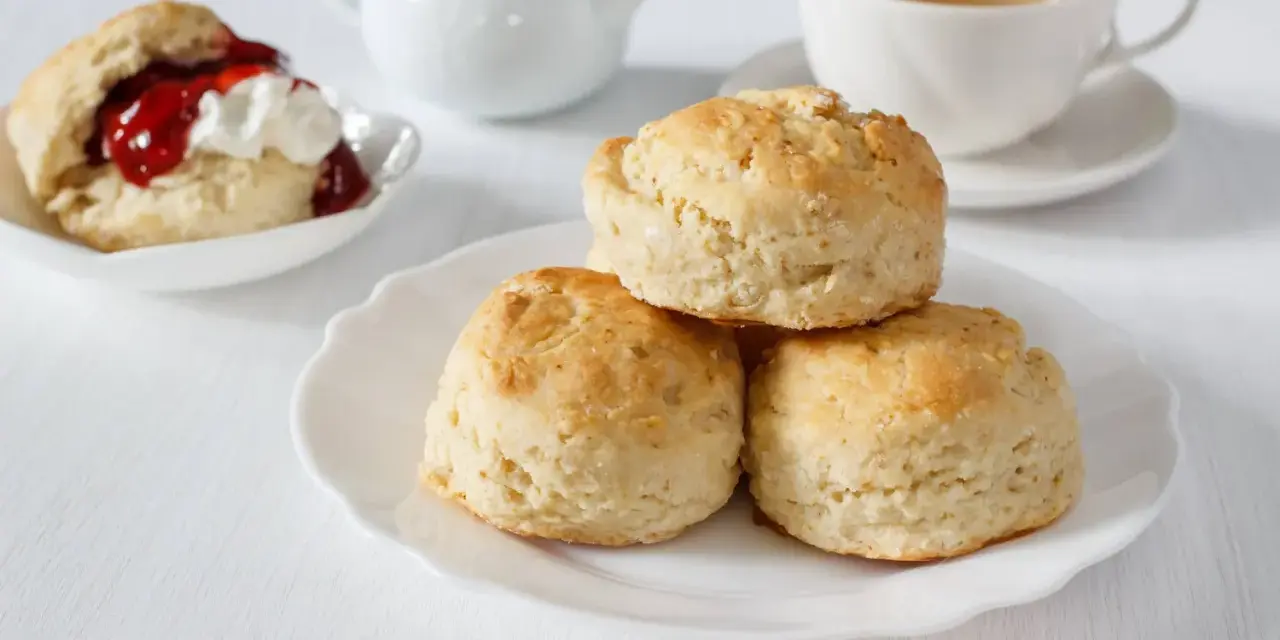 Goldbraune Scones, ein Klassiker zum Tee. Sie sind kleine, süße Gebäckstücke, die oft mit Marmelade und Sahne serviert werden.