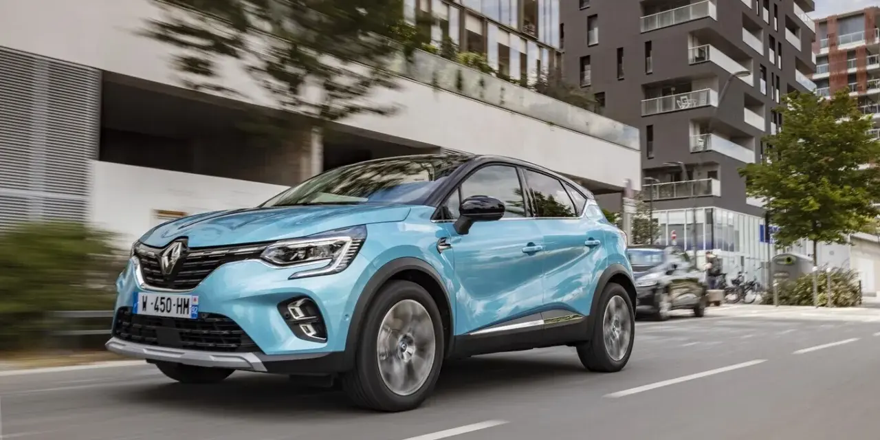 Un Renault Captur azul circula por una ciudad moderna. Es un híbrido no enchufable, eficiente y elegante.