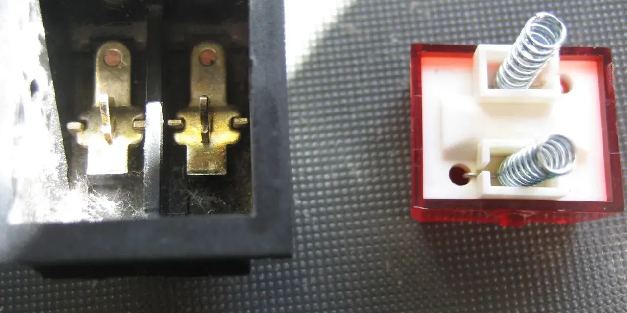 Detalle del interruptor de paso por dentro: contactos metálicos en un lado y resortes en el otro, listos para conectar.