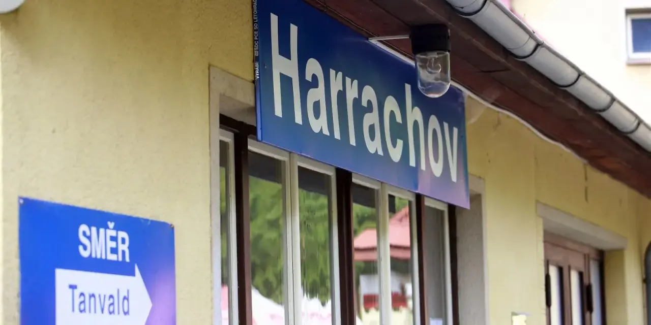 Tabliczka "Harrachov" nad oknami dworca. Obok znak kierunkowy "Směr Tanvald". Pociąg Szklarska Poręba Harrachov czeka na pasażerów.