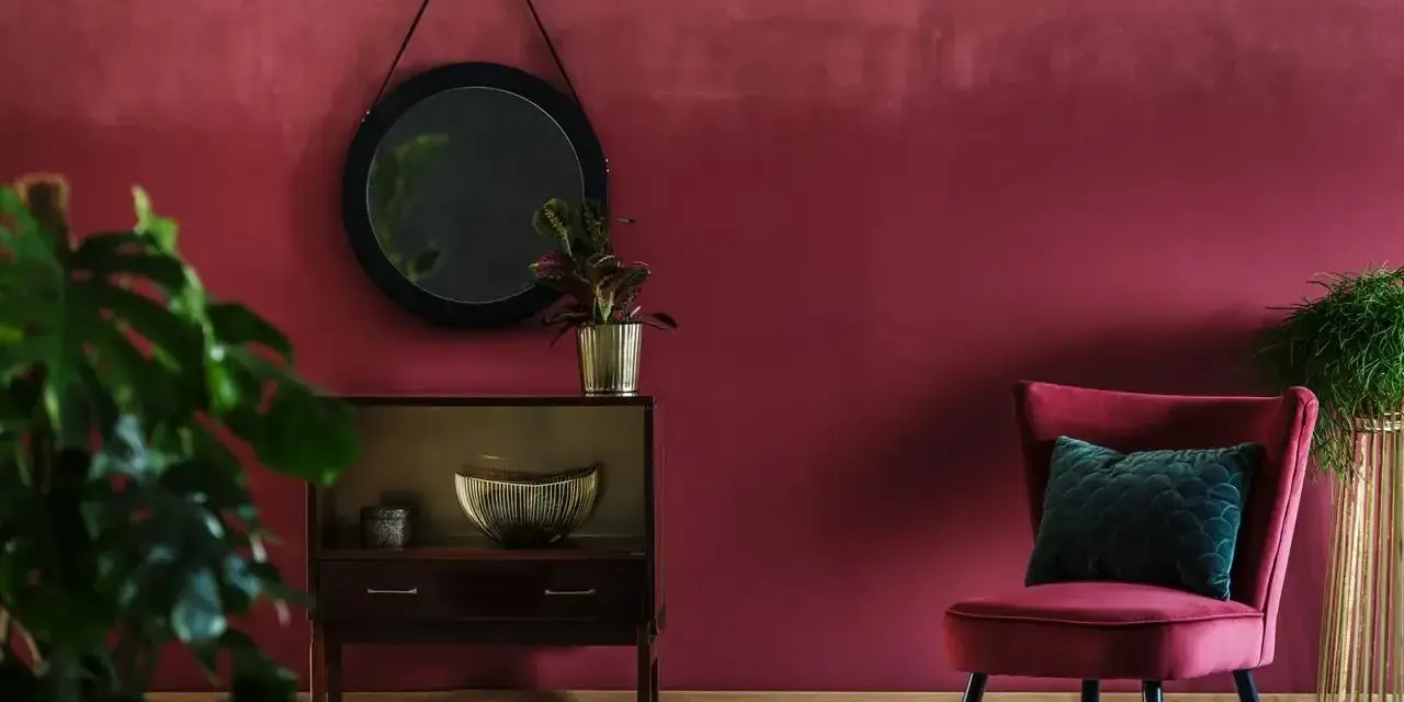 Eleganckie wnętrze w odcieniu **kolor burgundowy**. Aksamitny fotel, lustro i stylowa komoda tworzą przytulną atmosferę.