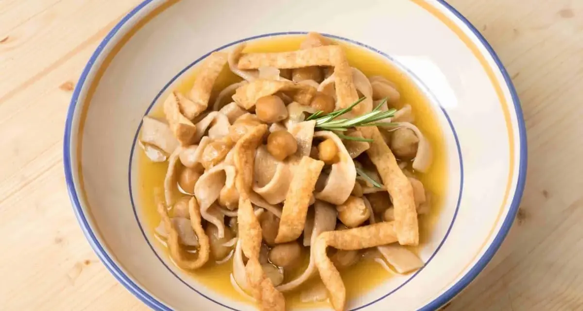 Un piatto di ciceri e tria, pasta fresca con ceci e sfoglie fritte, guarnito con rosmarino.