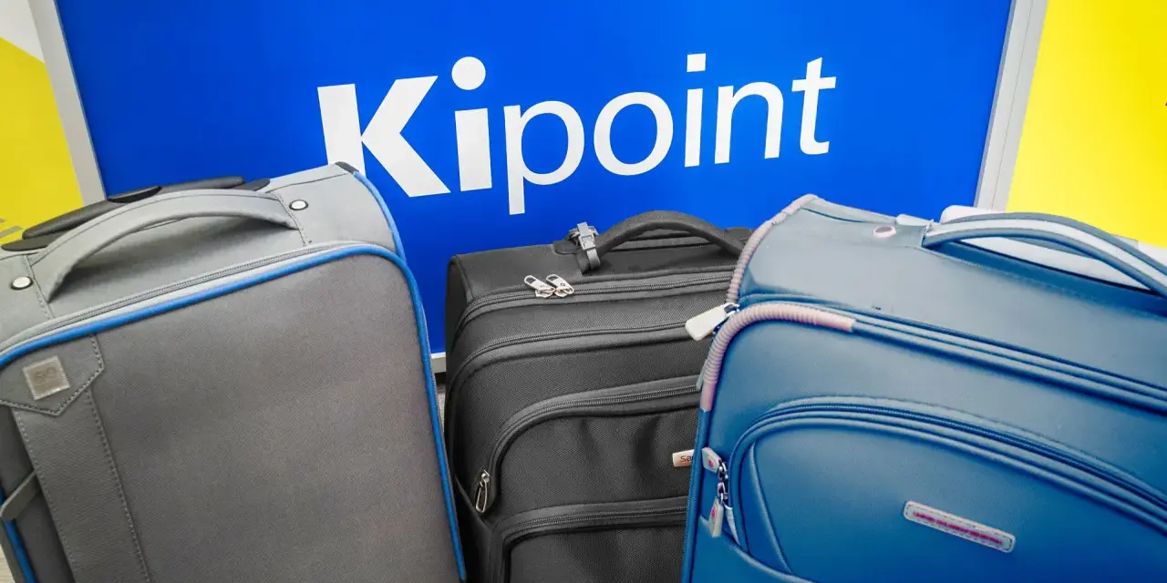 Three suitcases in front of a blue sign with "Kipoint" in white letters.