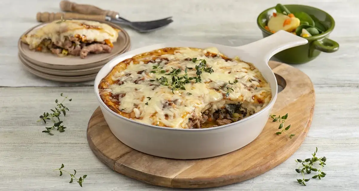Zapiekanka makaronowa z mięsem mielonym w sosie śmietanowym, posypana serem i ziołami, podana z sałatką.