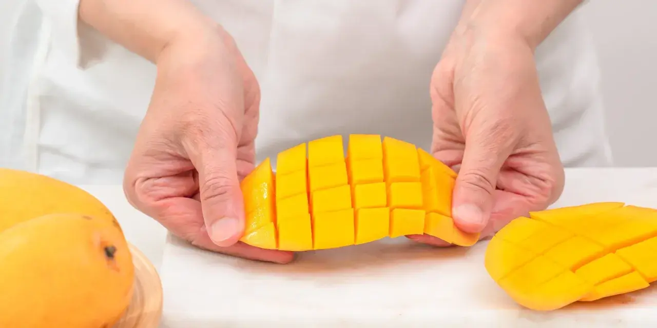 Ręce kroją dojrzałe mango na kostki. Czy mango ma pestkę? Tak, ale jej nie widać, bo jest w środku.