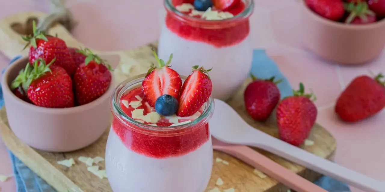 Zwei Gläser mit cremigem Joghurt und Erdbeersoße, garniert mit frischen Erdbeeren und Blaubeeren. Ein schneller Nachtisch mit Erdbeeren, der Lust auf mehr macht.