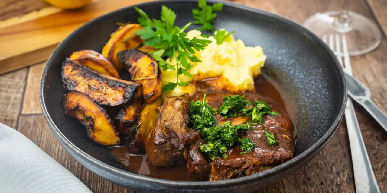 Herzhaftes Osso Buco, eine **beinscheibe italienisch** zubereitet, serviert mit cremigem Kartoffelpüree und gerösteten Kartoffelspalten.
