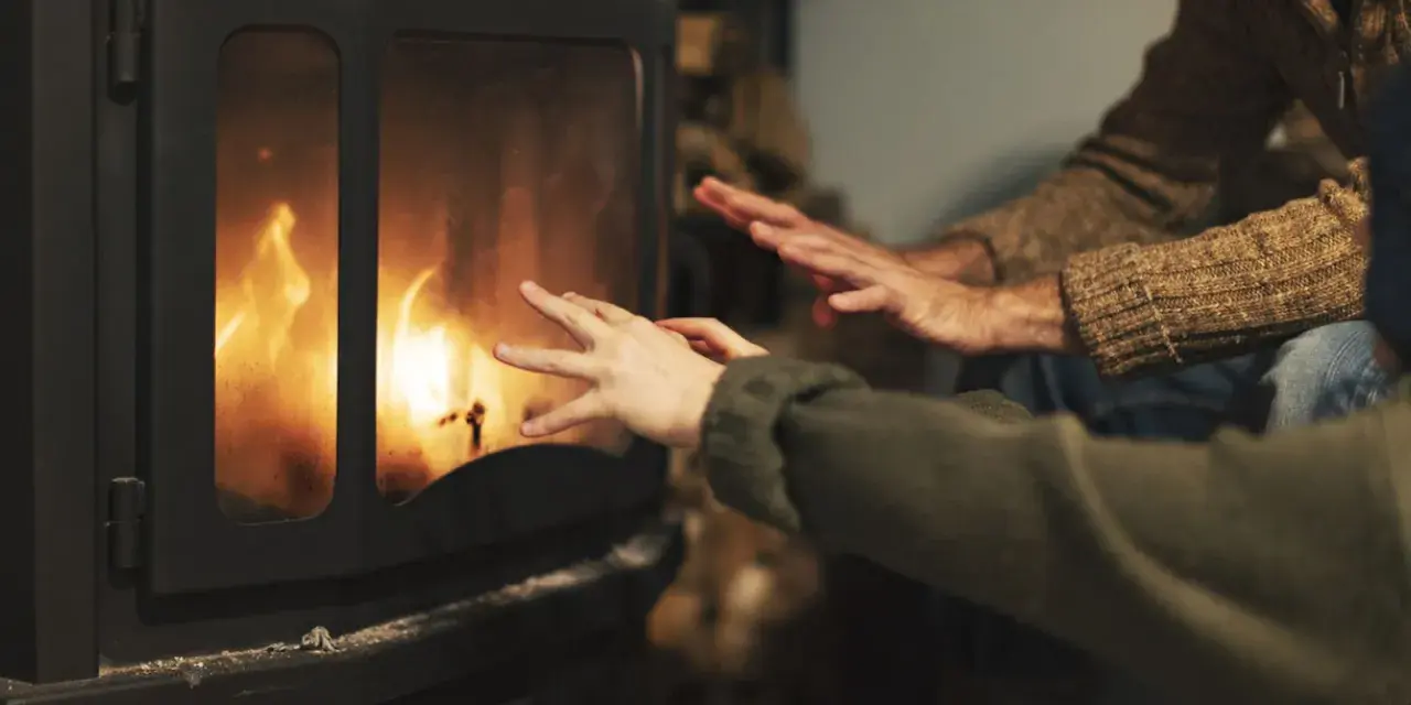 Manos calentándose frente a una chimenea con llamas danzantes. Los tubos de aire de la chimenea ayudan a distribuir el calor.