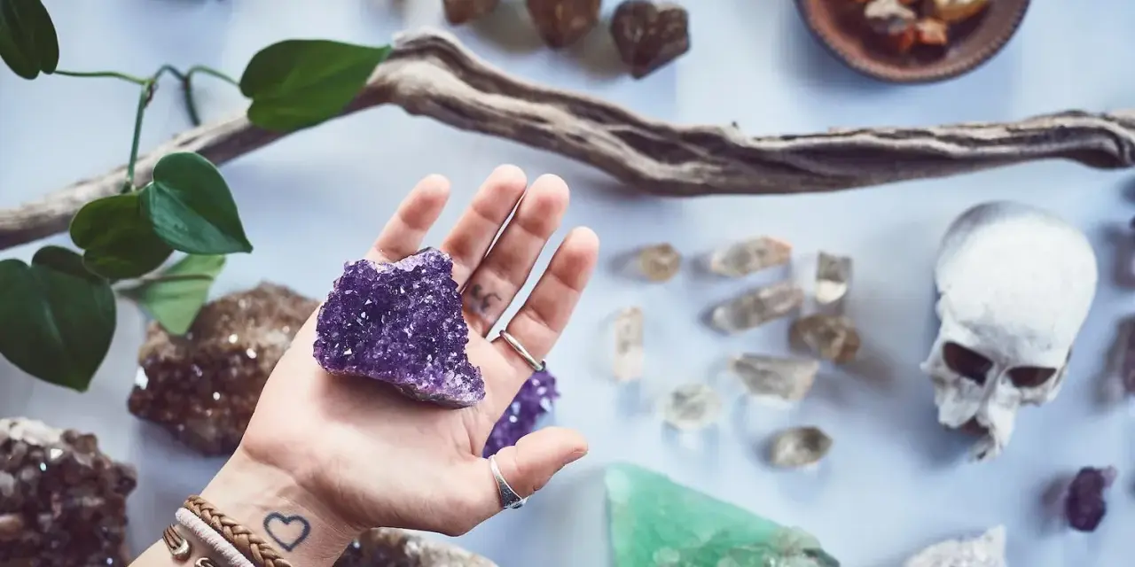 Mano sostiene amatista, rodeada de piedras y un cráneo. Un conjunto de piedras contra el mal de ojo y la envidia.