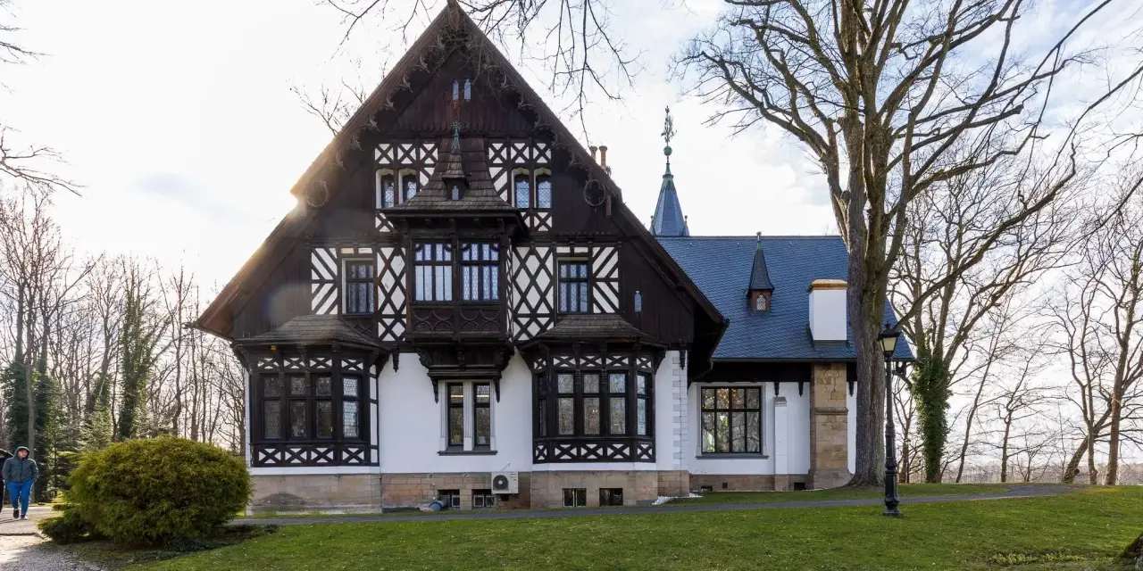 Pałac myśliwski w Promnicach, z charakterystyczną architekturą szachulcową i zdobieniami, otoczony drzewami.