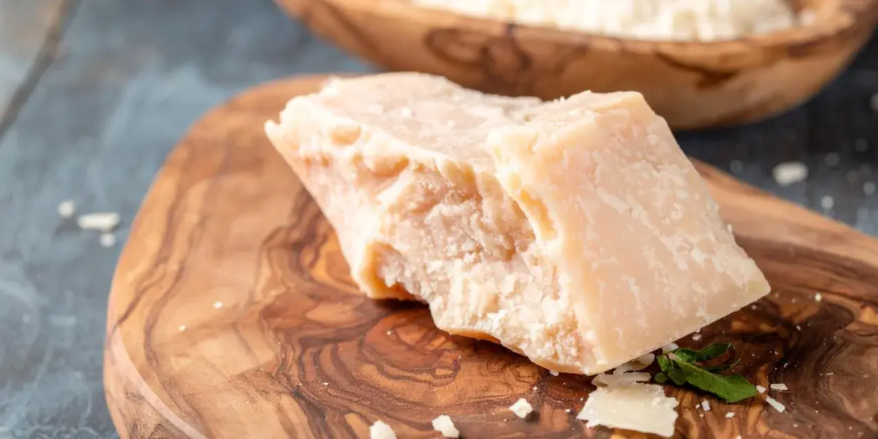 Kawałek twardego sera Grana Padano na desce z oliwnego drewna. Czy Grana Padano to parmezan? To pytanie często zadawane przez miłośników włoskich serów.
