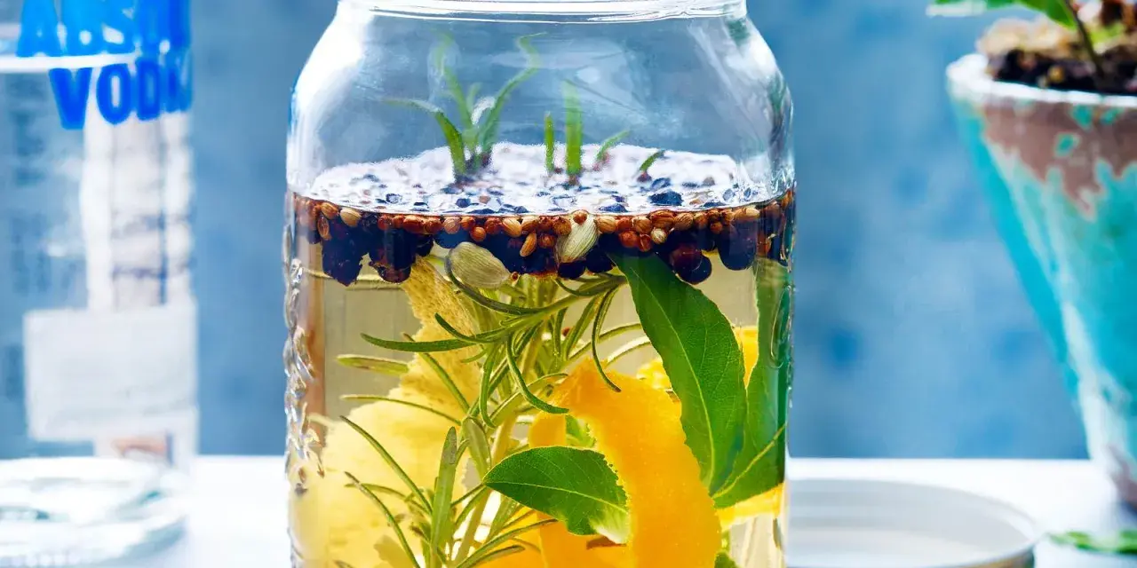 Ein Glas mit Zutaten für ein Sloe Gin Rezept: Wacholder, Zimt, Zitronenschale, Rosmarin und Lorbeerblätter in Alkohol.
