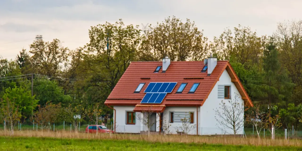 Nowoczesny dom energooszczędny z panelami słonecznymi na dachu, otoczony zielenią.
