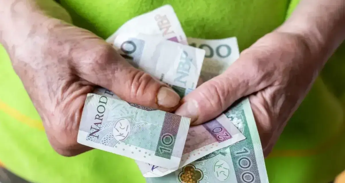 Dłonie trzymają polskie banknoty. Nowe zasady przyznawania renty socjalnej mogą wpłynąć na finanse wielu osób.