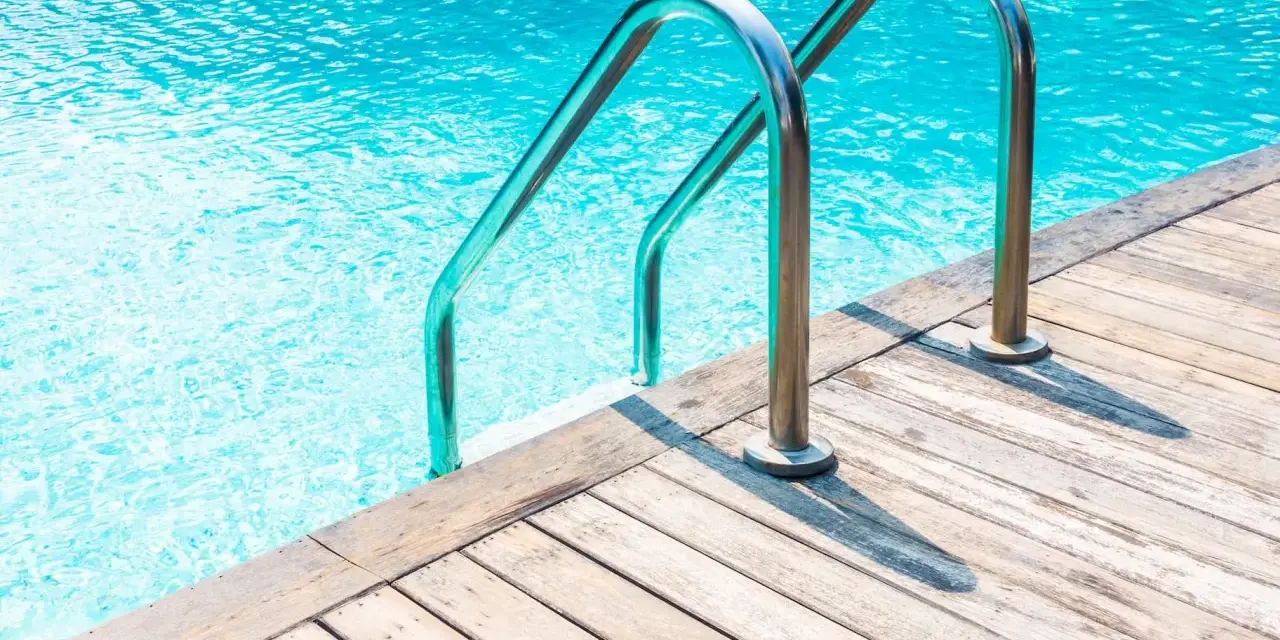 Escalera de piscina de obra con barandillas cromadas sobre tarima de madera. ¿Cuánto cuesta una piscina de obra?