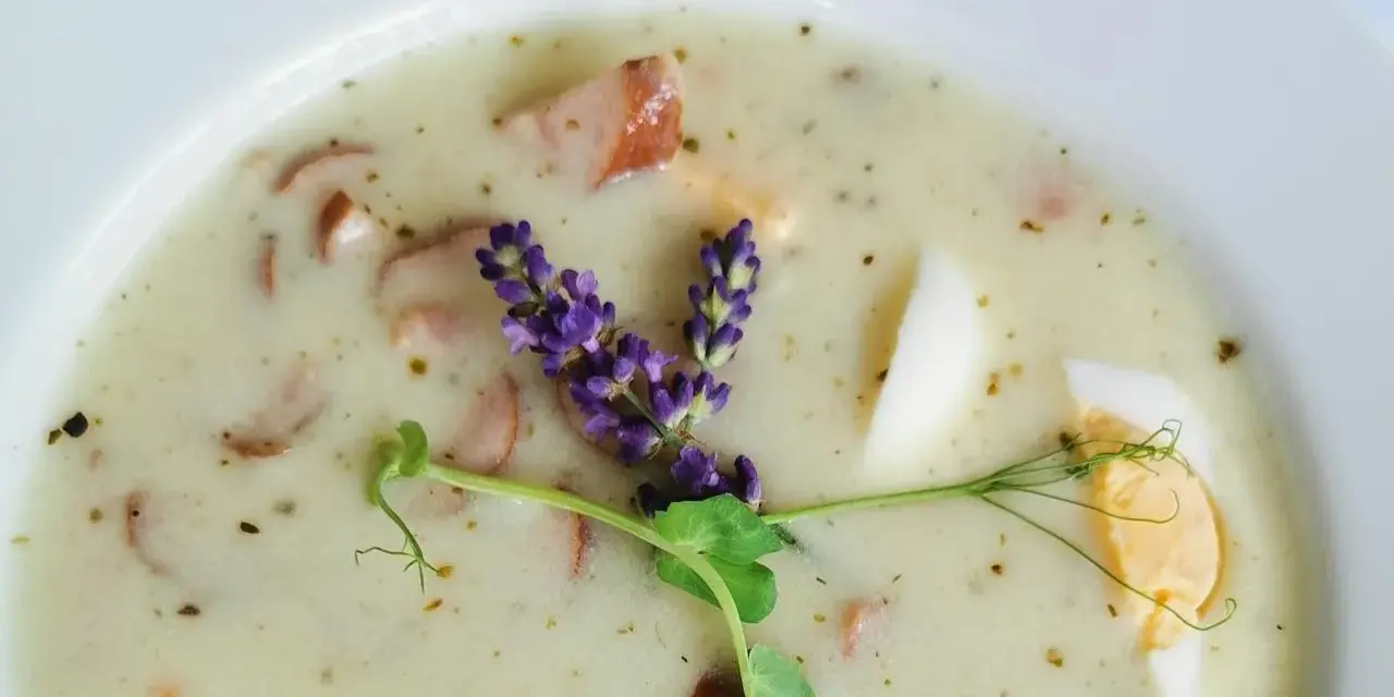 Aromaticzny żurek z kiełbasą i jajkiem, ozdobiony gałązką lawendy i kiełkami.