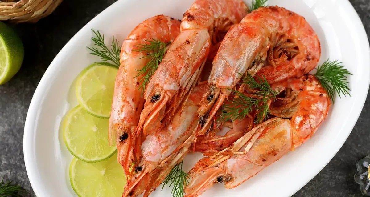 Plato blanco con langostinos cocidos, rodajas de limón y eneldo. Ideal para recetas con langostinos.