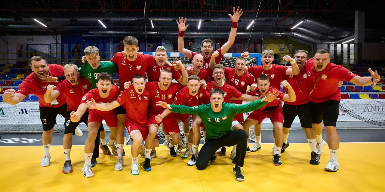 Drużyna piłkarzy ręcznych w czerwonych strojach świętuje zwycięstwo. Wśród nich Krzysztof Zimny, bramkarz w zielonym stroju, klęczy z wyciągniętymi rękami.