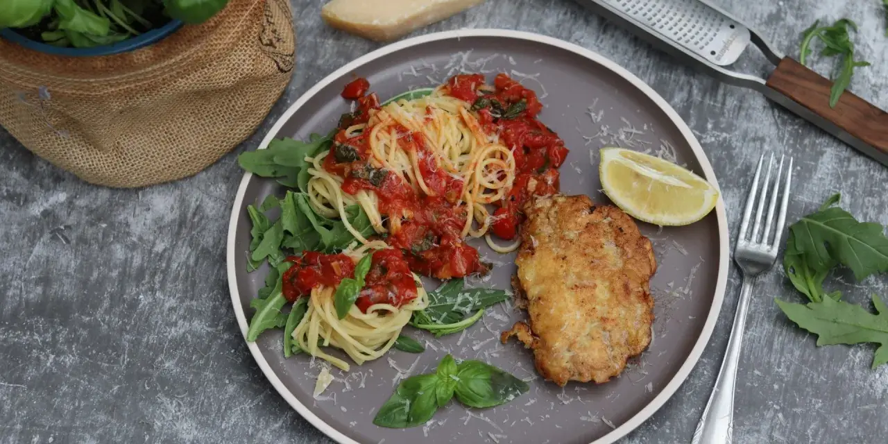 Piccata Milanese: goldbraunes Schnitzel mit Spaghetti in Tomatensauce, garniert mit Rucola und Zitrone.