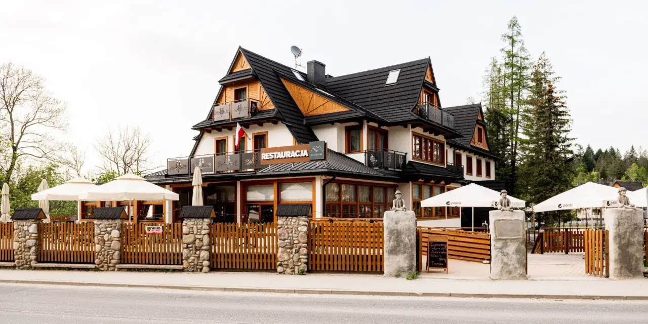 Szukasz miejsca, gdzie zjeść w Kościelisku? Ta restauracja z drewnianym ogrodzeniem i białymi parasolami zaprasza na góralskie smaki.