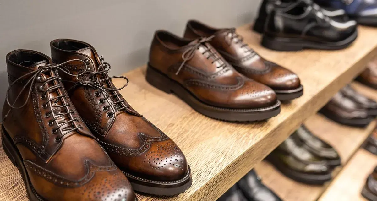 Scarpe marchigiane famose: eleganti stivaletti e stringate in cuoio marrone, con dettagli traforati, su uno scaffale di legno.