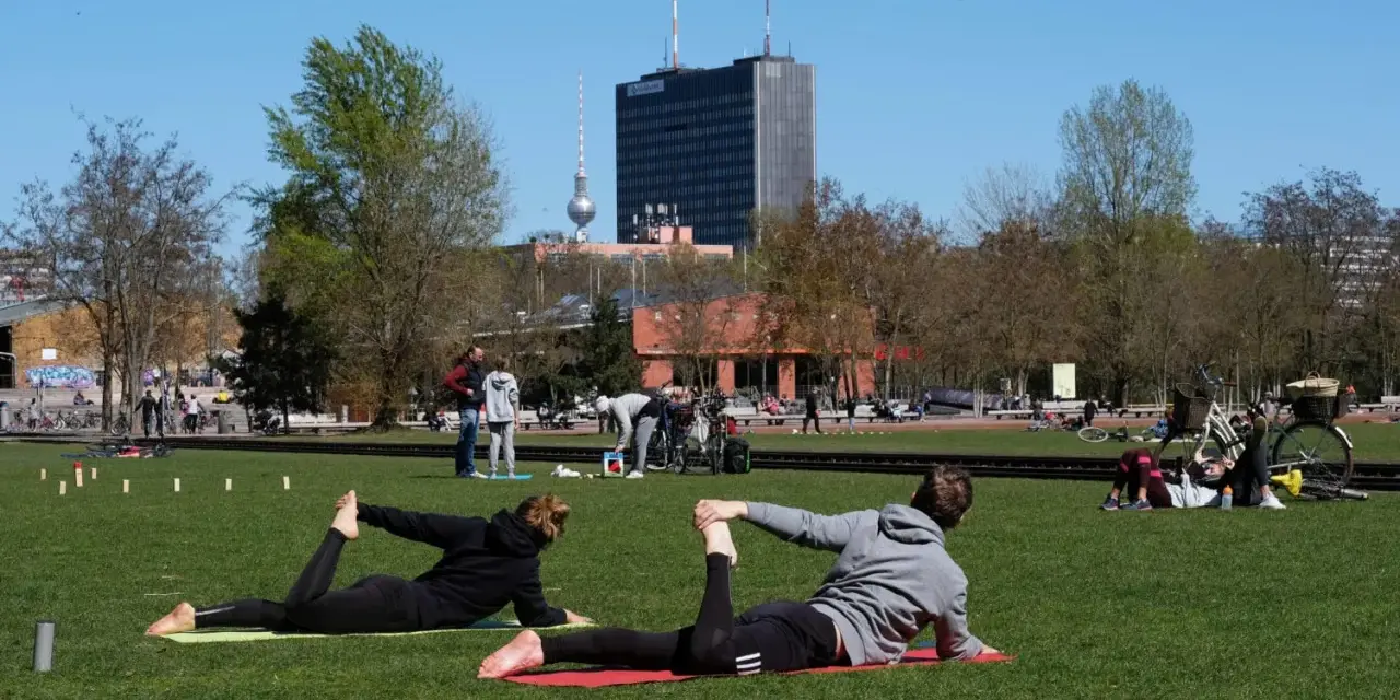 Menschen machen Yoga und entspannen sich im Park. Ein sonniger Tag für Sport in Berlin mit dem Fernsehturm im Hintergrund.