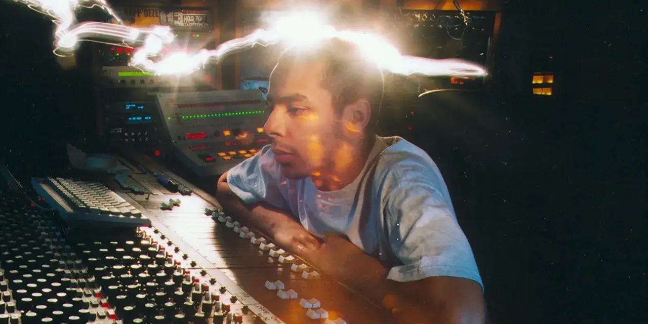 Un disc jockey célèbre, concentré, manipule une console de mixage dans un studio d'enregistrement, baigné de lumières vives.