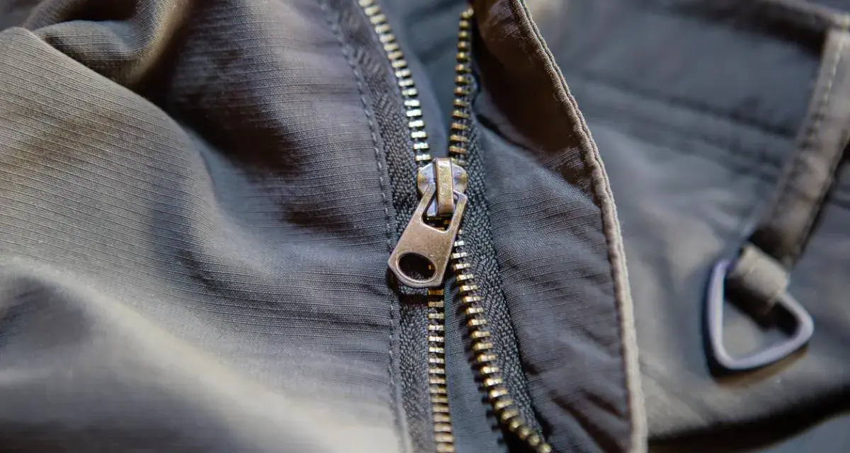 Detalle de una cremallera de chaqueta que se ha salido, mostrando el cursor metálico y los dientes.