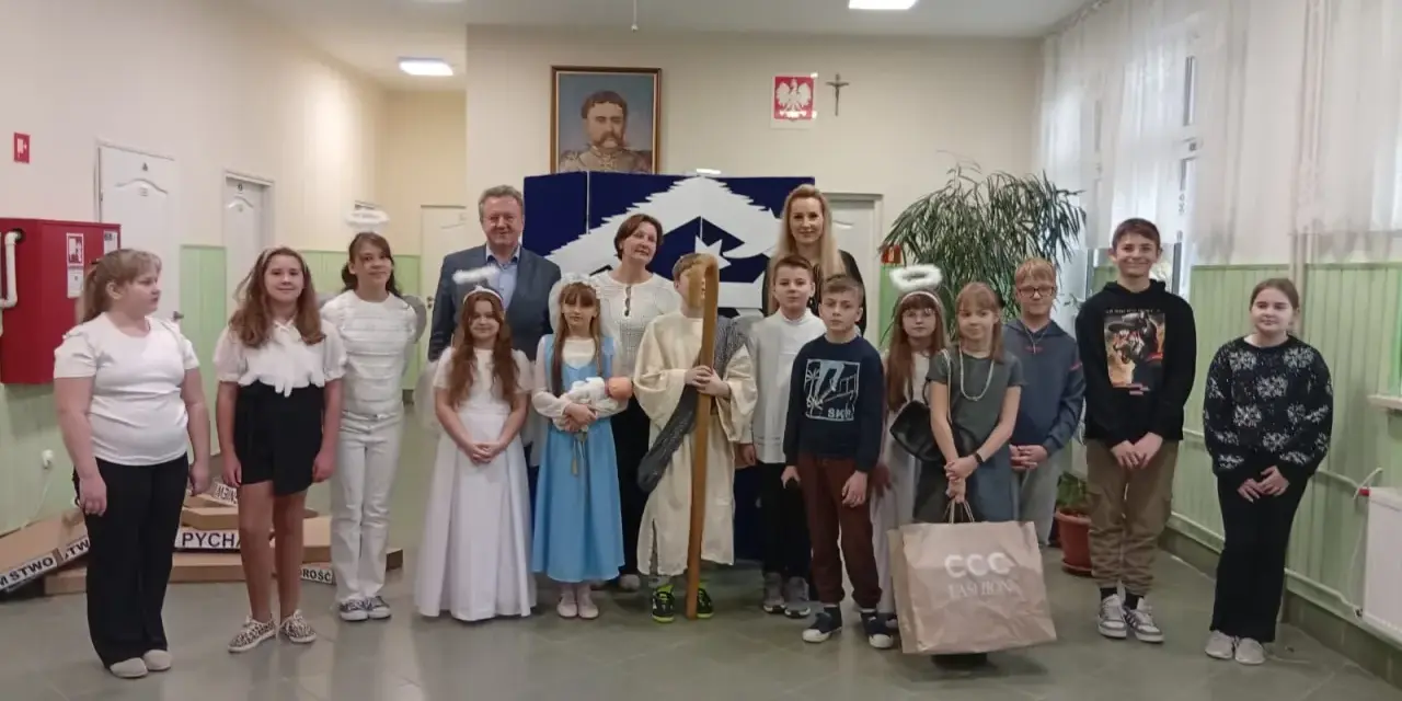 Dzieci w strojach aniołów i pasterzy, odgrywające baśń o dobrym synku. W tle portret i dekoracje.