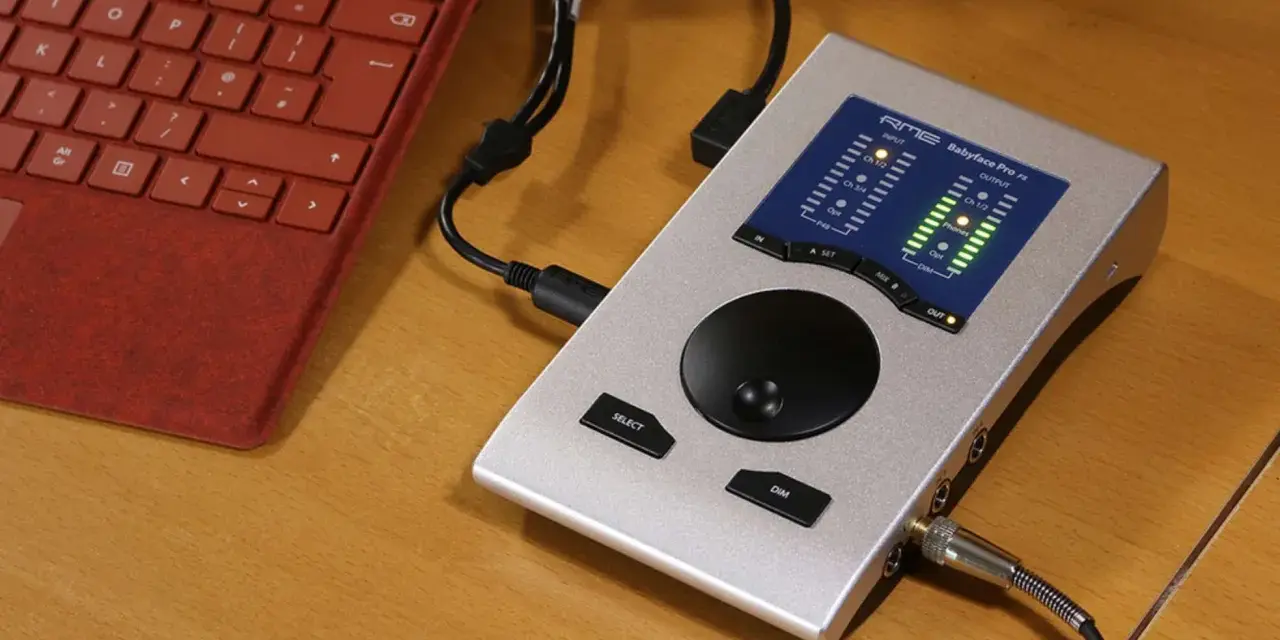 Srebrny interfejs audio RME Babyface Pro FS podłączony do czerwonej klawiatury. Idealny do mobilnego studia.
