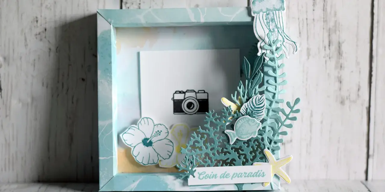 Un cadre photo en bois décoré sur le thème marin avec une méduse, des poissons, des fleurs et une petite caméra.
