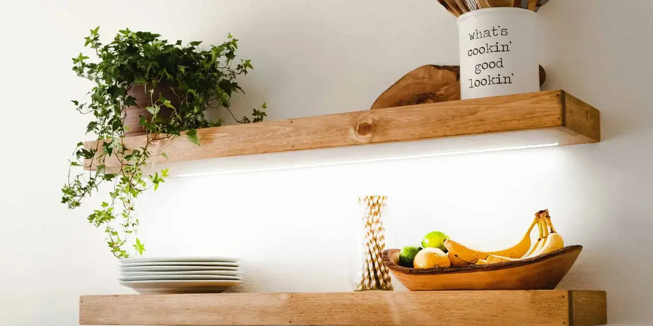 Estantes de madera con iluminación LED oculta, ideal para saber como colocar tiras led en estantes. Exhiben plantas, vajilla y frutas.