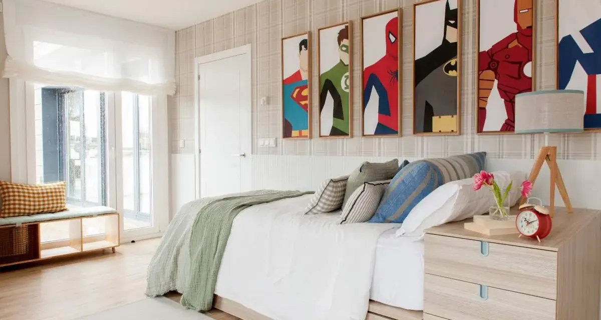 Habitación adolescente chico con cuadros de superhéroes, cama blanca con mantas verdes y cojines, mesita de noche de madera y ventana grande.