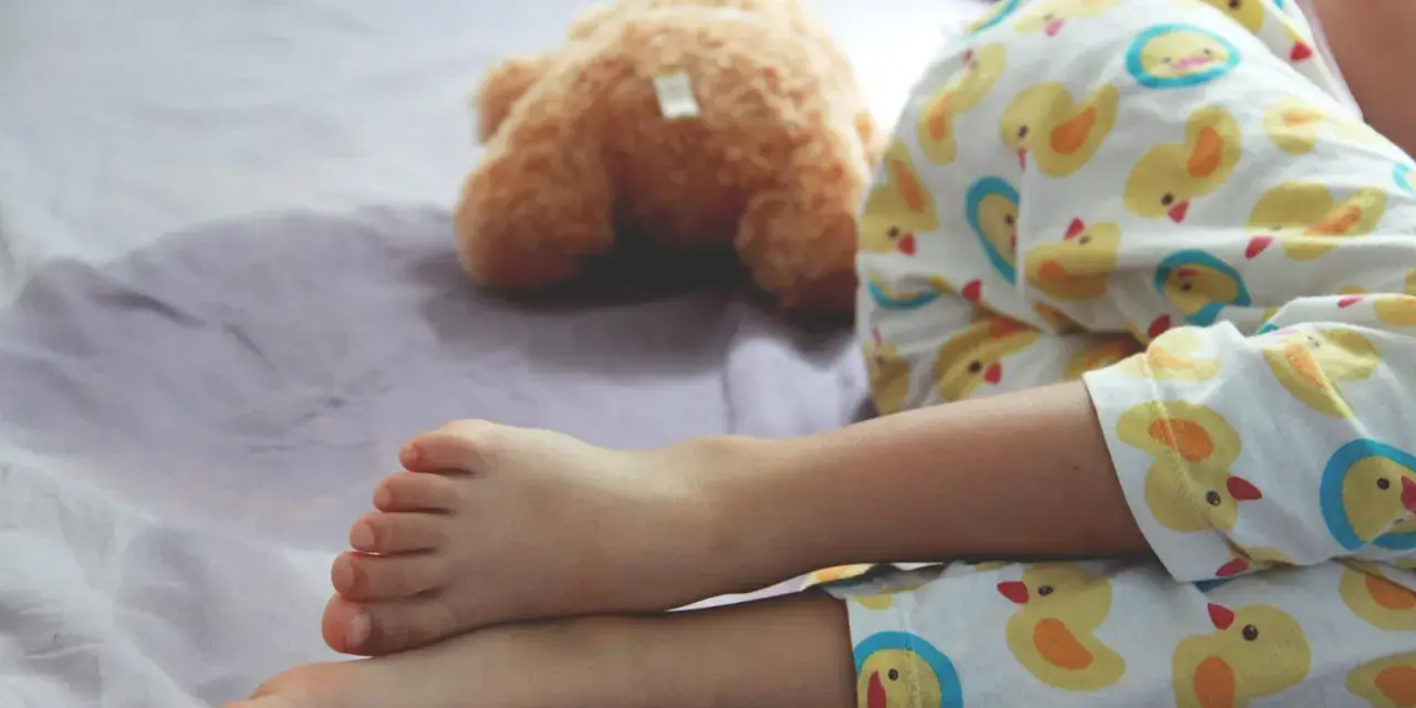 Ein Kind schläft im Pyjama mit Entenmuster, ein Teddybär liegt daneben. Es ist ein friedlicher Moment, in dem das Kind nachts ein und merkt es nicht.