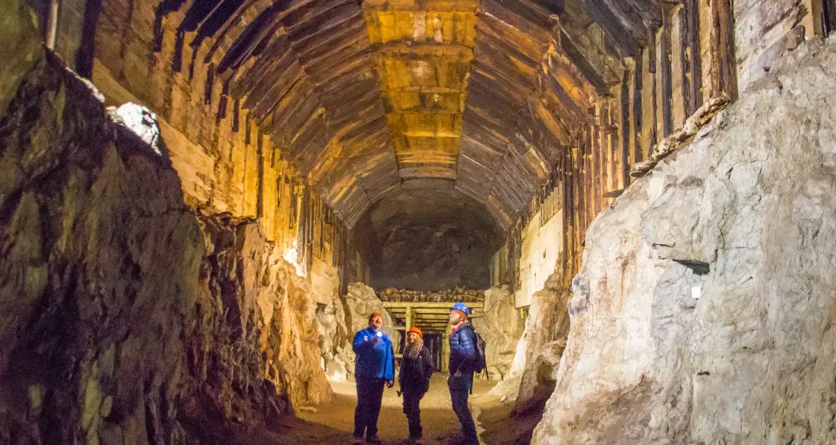 Zwiedzanie Kompleksu Riese: trzej turyści w kaskach oświetlają latarkami mroczny, drewniany tunel.