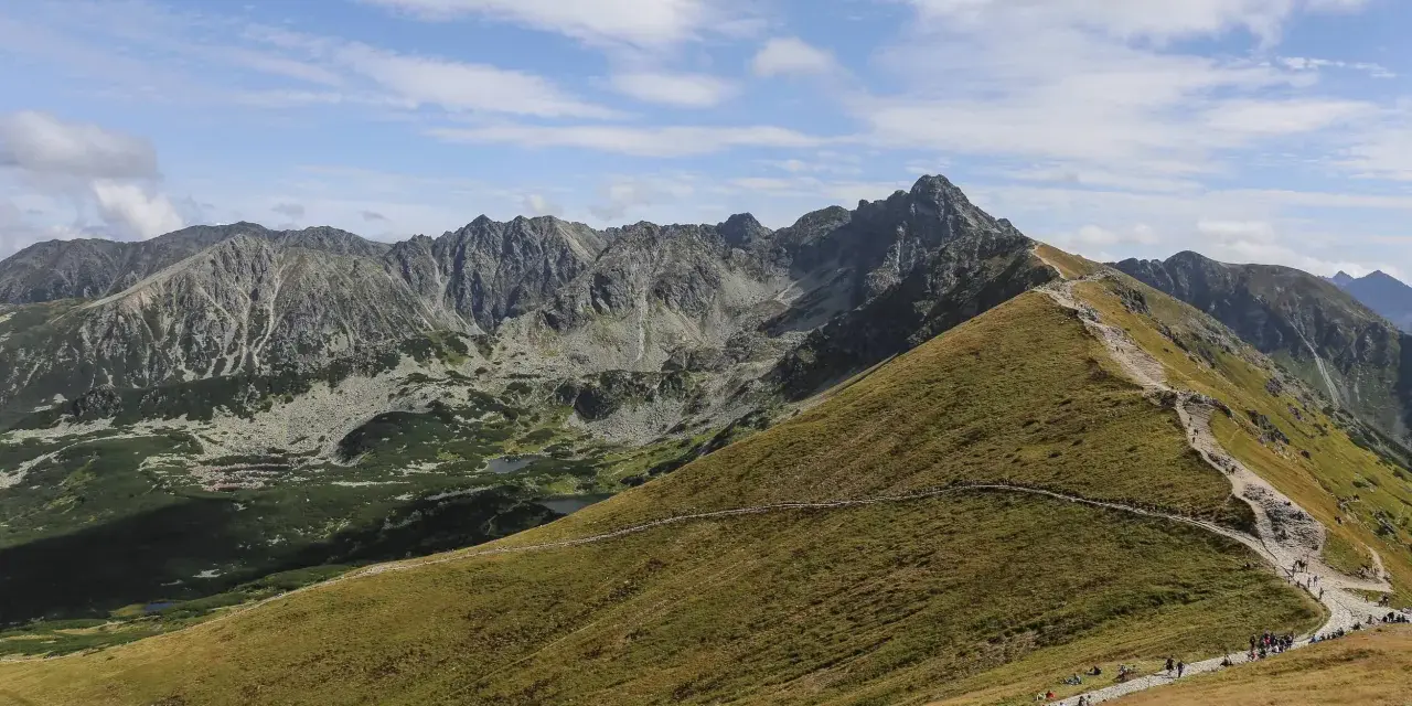 Szlak na Kasprowy Wierch jest popularny, turyści wędrują kamienistą ścieżką pośród zielonych zboczy Tatr.