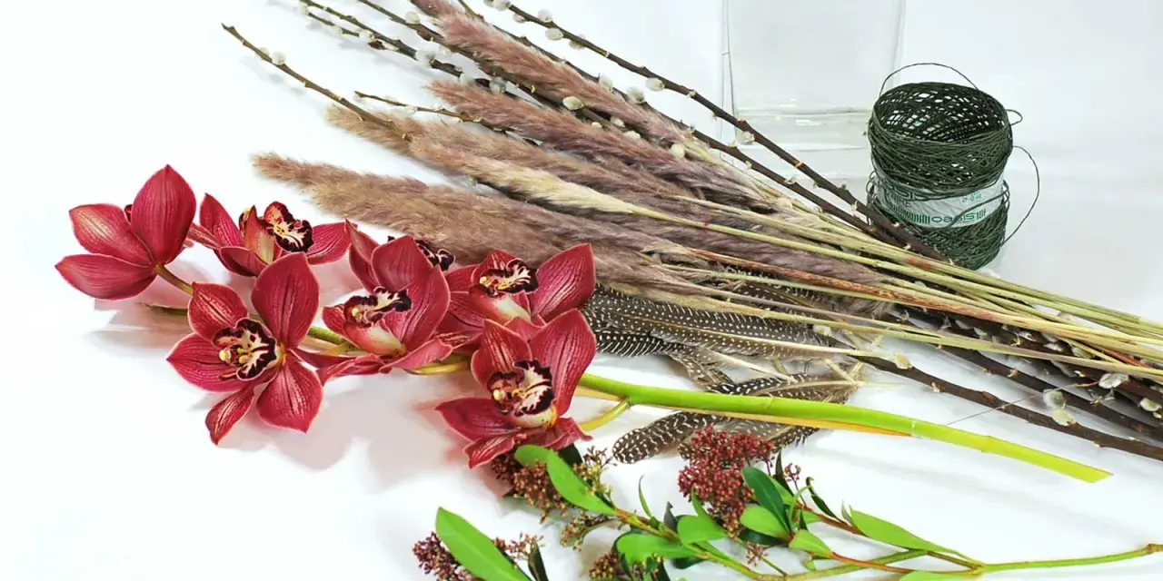 Ciemnoróżowe orchidee, trawy, pióra i gałązki tworzą kompozycję zrównoważoną.