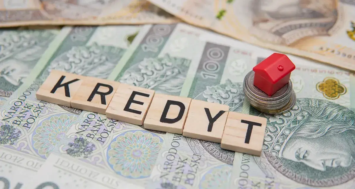Litery układające słowo "KREDYT" na banknotach. Mały czerwony domek na stosie monet symbolizuje pomoc w spłacie kredytu, np. z funduszu wsparcia kredytobiorców.