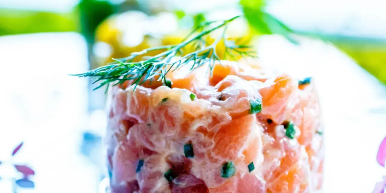 Tartare di salmone fresco, finemente tagliato e condito, guarnito con aneto. Un piatto leggero e saporito.