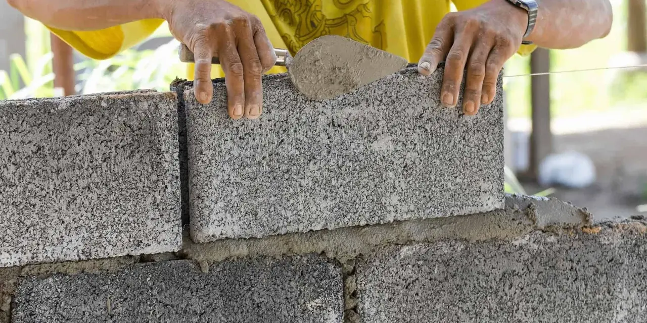 Murarz układa bloczek betonowy, sprawdzając jego wymiary.