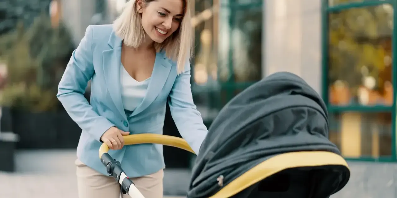 Uśmiechnięta kobieta w eleganckim stroju, z wózkiem dziecięcym, symbolizuje powrót do pracy po macierzyńskim.