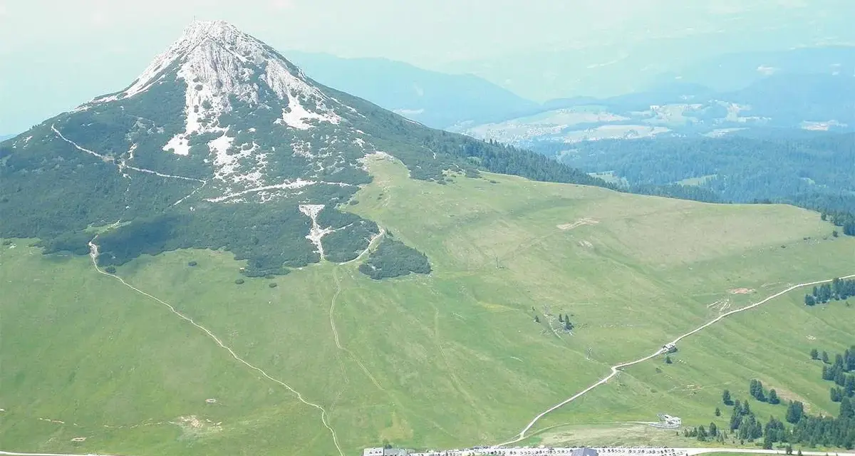 Panoramica delle malghe al Passo Lavazè, con un imponente monte sullo sfondo e sentieri che si snodano tra prati verdi.