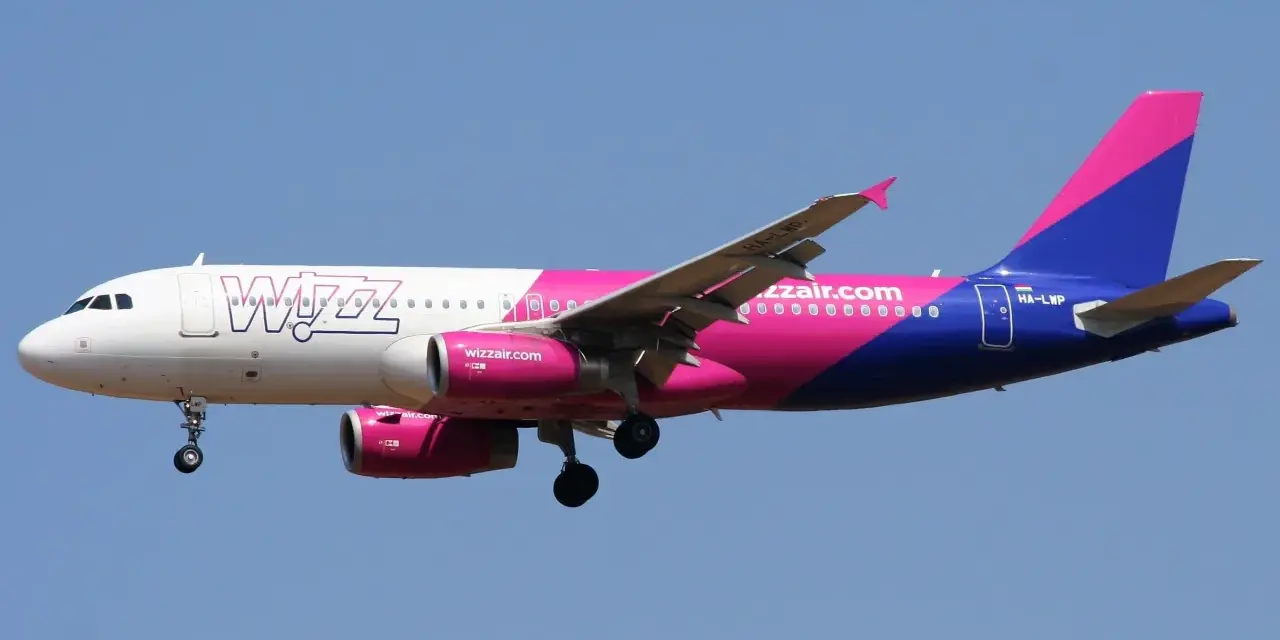 Samolot Wizz Air z różowo-fioletowym ogonem leci na tle błękitnego nieba. Sprawdź wizz discount club cena i leć taniej!