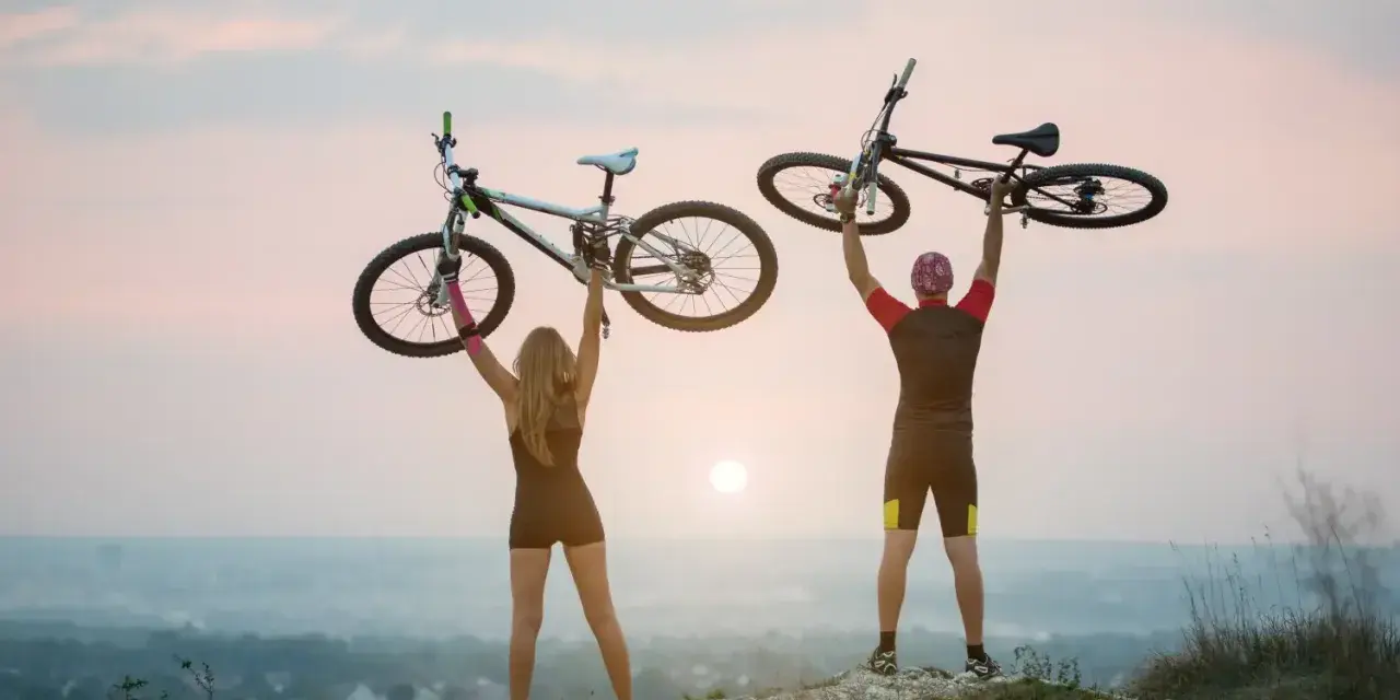 Para rowerzystów świętuje na szczycie, unosząc rowery. To idealny moment na odkrywanie najpiękniejsze odcinki z green velo.