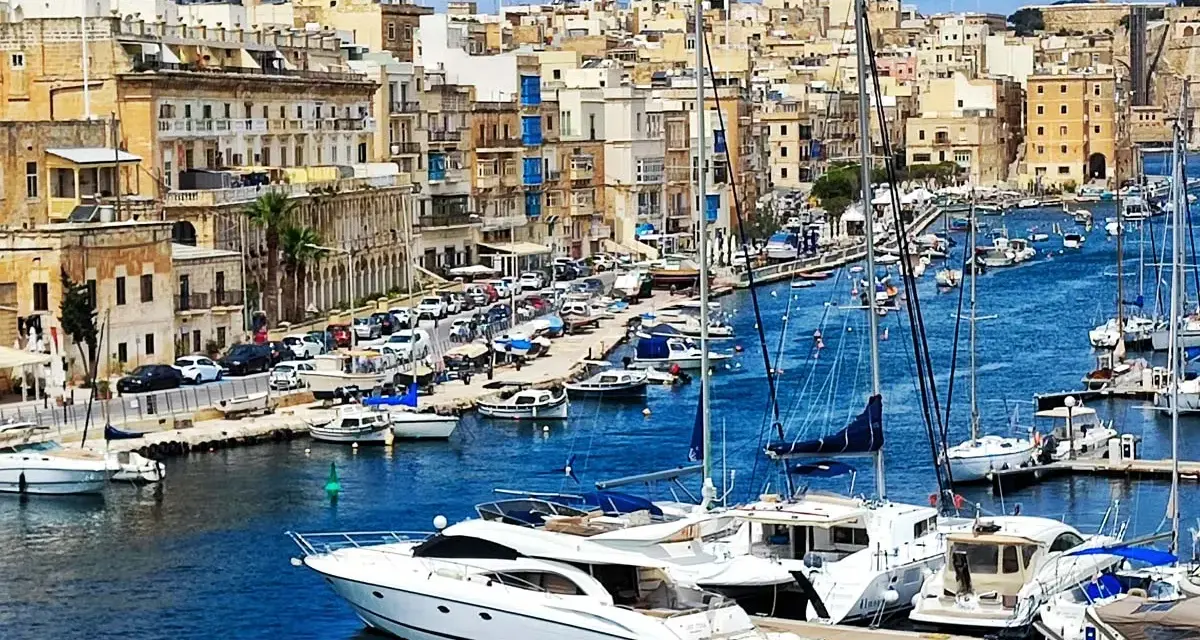 Malta plan zwiedzania: malowniczy port z łodziami i zabytkowymi budynkami w tle.