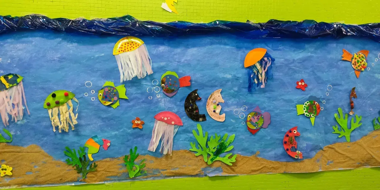 Un colorido mural de animales marinos infantiles con peces, medusas y caballitos de mar nadando en un mar azul, sobre arena.