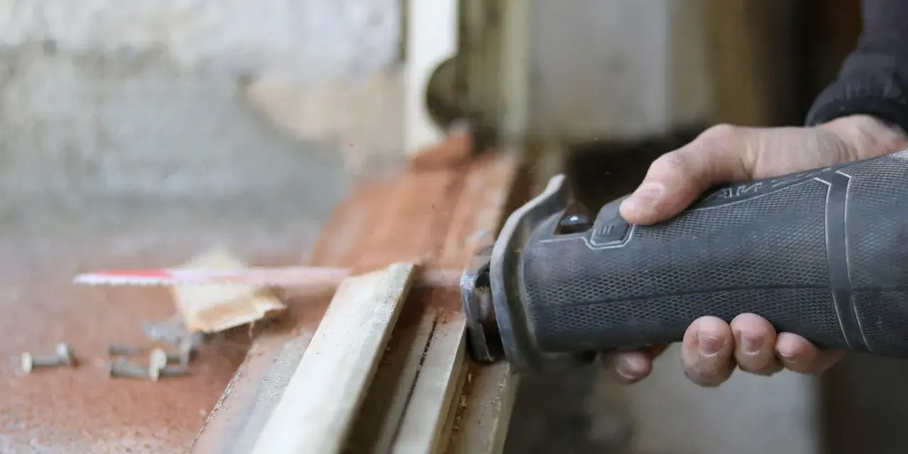 Main d'un artisan utilisant une scie sauteuse pour la dépose totale d'une fenêtre. Estimation du prix pose fenêtre dépose totale.