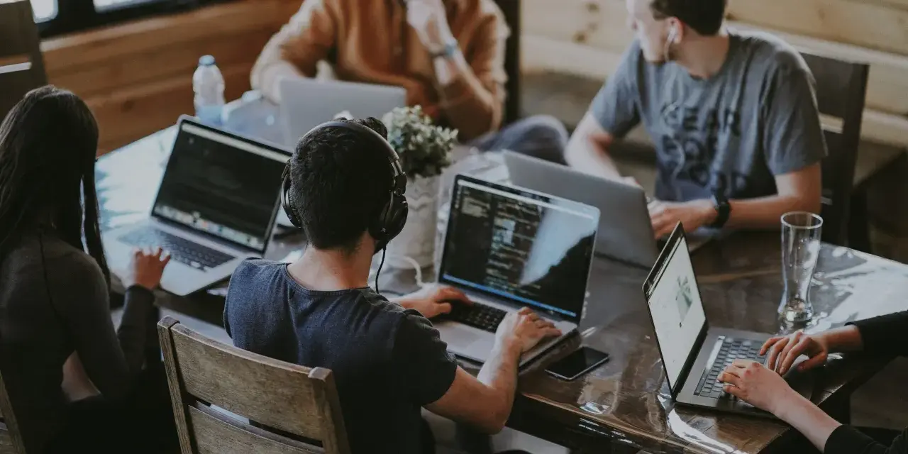 Un grupo de personas trabaja en sus portátiles en una mesa. Uno de ellos, con auriculares, parece concentrado en su pantalla, quizás buscando la clave del modelo 190.
